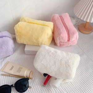 Flat lay of macaron-colored plush cosmetic bags in white, yellow, pink, and purple shades