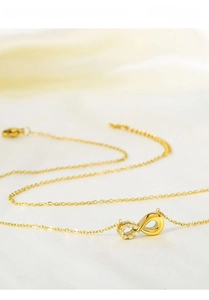 Close-up of a gold infinity necklace with white zircon accents on white silk fabric
