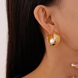 Close-up of gold mesh texture earring with a white pearl on a model's ear