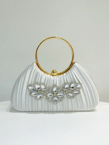 Macro detail of white pleated evening tote bag with gold ring handle and crystal butterfly