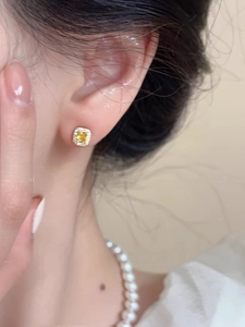 Close-up of square yellow gemstone stud earring with halo crystals on ear