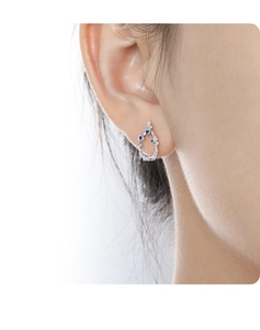 Detailed close-up of a silver branch-shaped earring with small blue gemstone accents