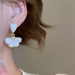 Vue détaillée des boucles d'oreilles fleur en émail blanc et dorure sur le mannequin
