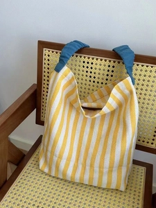 Casual yellow and white striped canvas tote bag with blue handles on a wooden chair