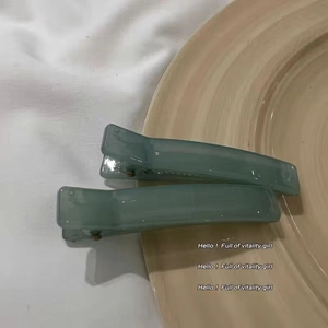 Close-up of two grey-green jelly-colored acrylic square hair clips on fabric