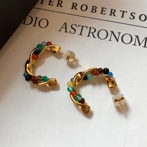Detail of golden C-shaped twisted earrings with colorful beaded stones and silver needles