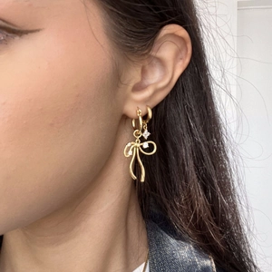 Close-up of gold plated bow pendant earrings with zircon stones worn by a model