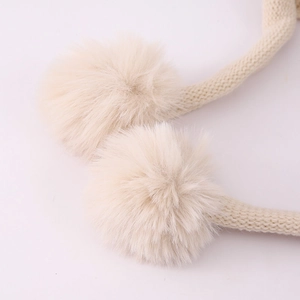 Detailed close-up of fluffy off-white faux fur pom-poms and soft knitted strings on a baby hat