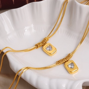 Double-layered gold snake chain necklace with heart crystal pendant on ceramic shell tray