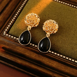 Close-up of vintage gold flower earrings with black teardrop gemstones on velvet