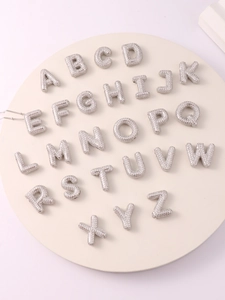 Close-up of balloon style initial pendants with zircon stones on a white stand