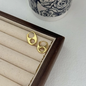 Close-up of golden double-loop earrings on a beige tray with a polished mirror finish