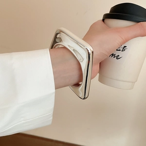 Close-up of a silver polished geometric square bangle styled with a white blazer