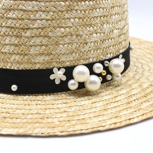 Detail of straw hat with black ribbon featuring pearls, gold beads and flower charms