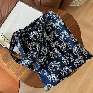 Detail of navy blue canvas tote bag featuring all-over white animal embroidery on a wooden table