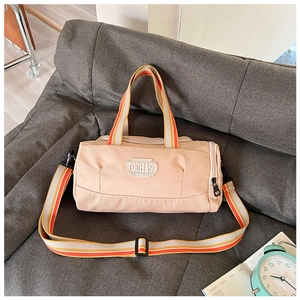 Detail of beige cylinder sports bag with TOCHASO patch and striped handles on sofa