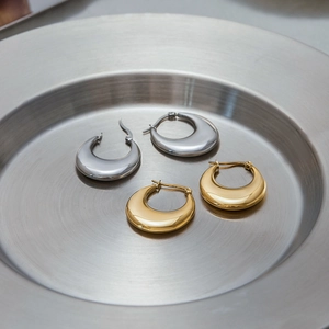 Macro view of gold and silver chunky stainless steel hoop earrings on a metal tray
