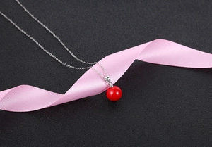 Macro shot of minimalist silver necklace with red pearl pendant on dark textured background