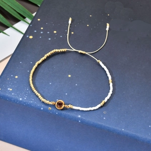 Macro detail of adjustable beaded bracelet with purple zircon and gold beads on blue box