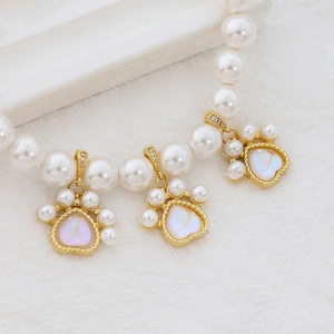 Macro shot of gold-plated cat paw charms with iridescent heart on pearl necklace