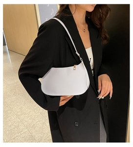 Minimalist white leather underarm bag with gold zipper shown on a black suit blazer