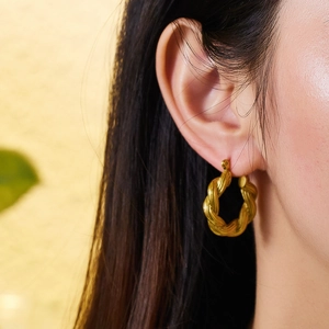 Close-up of gold twisted rope hoop earring worn by a model showcasing high-end texture