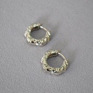 Macro view of silver hoop earrings featuring irregular liquid metal and lava texture details