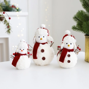 Three plush Christmas snowman figures with red scarves and hats in warm festive setting
