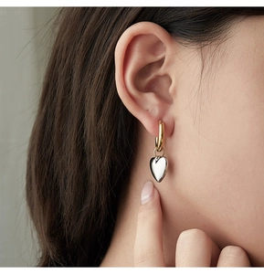 Detail of two-tone heart pendant hoop earring in gold and silver on a model ear