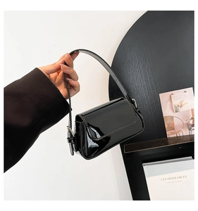 Close-up of black glossy patent leather shoulder bag held by a model in a minimalist setting