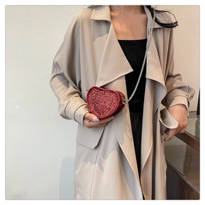 Red sequin heart-shaped mini crossbody bag with silver chain strap worn on beige trench coat