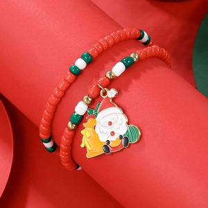 Macro detail of Christmas beaded bracelet with Santa Claus charm on festive red background