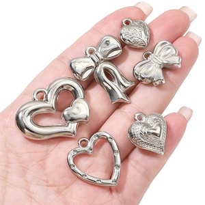 Silver CCB heart and bow pendants for DIY jewelry making held in hand for scale