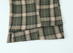 Détail rapproché du pantalon à carreaux vert et beige montrant la texture du tissu et l'ourlet