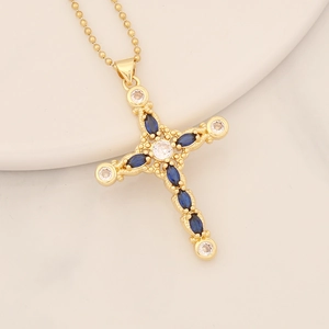 Macro detail of gold cross pendant with deep blue and clear gems on a white tray
