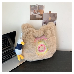 Detail of plush khaki tote with donut embroidery and cute duck charm on a desk