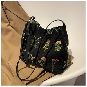 Detailed close-up of vibrant floral embroidery on a black canvas tote bag surface