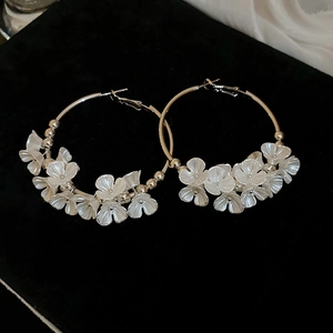 Detail view of gold hoop earrings with white flower charms on black velvet background