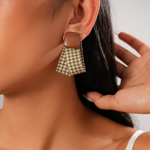 Detailed view of geometric leather earrings with houndstooth fabric texture on a model