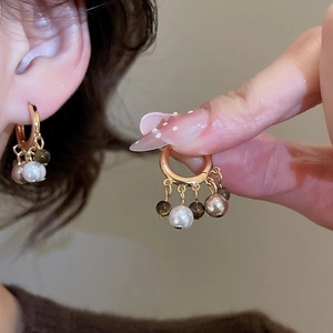 Detail of 18k gold-plated hoop earrings featuring natural tiger eye and pearl charms