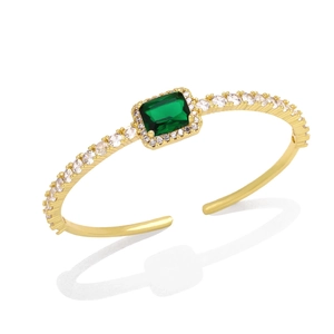 Macro shot of an open gold bangle featuring a green emerald-cut zircon and pave crystals