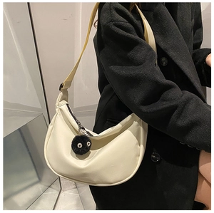Detail of a creamy white half-moon crossbody bag with a black plush soot sprite charm