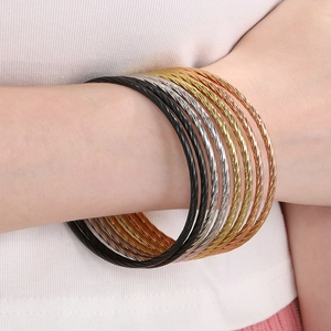 Stacked twisted wire bracelets in black, gold, silver, and rose gold on a model's wrist