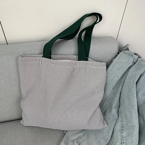 Detail of black and white striped canvas tote bag with dark green cotton handles on a sofa