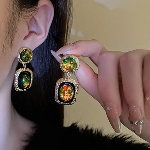 Détail de boucles d'oreilles géométriques dorées avec résine verte opalescente sur modèle