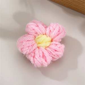 Handmade knitted pink flower hair clip accessory with yellow center on white desk