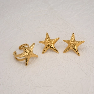 Macro detail of 18k gold plated starfish ring and earrings set on textured white fabric