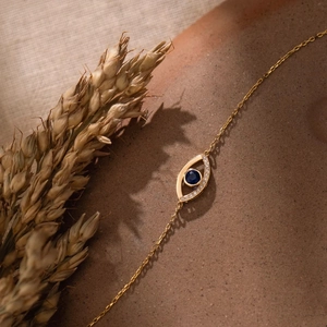 Detailed macro view of evil eye pendant with blue gemstone and gold chain on stone
