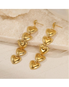 Close-up of golden heart drop earrings with beaded edges on a white stone background