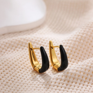 Close-up of 18K gold U-shaped earrings with black enamel finish on woven fabric